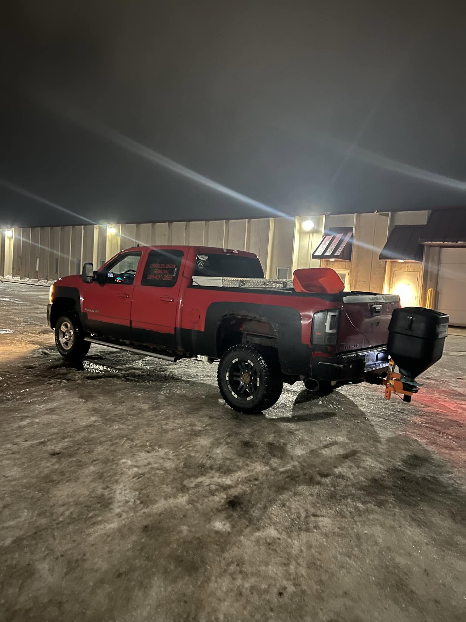 Charles Snow Removal truck with a salt spreader on an icy commercial lot at night